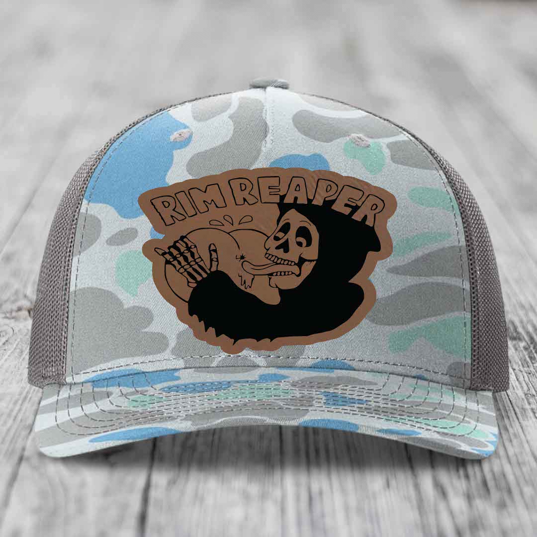 Camouflage trucker hat with brown leather patch featuring skull holding baseball bat and &