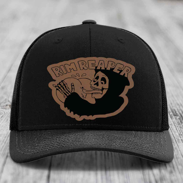 Black trucker hat with brown leatherette patch featuring skull holding baseball, text reads &