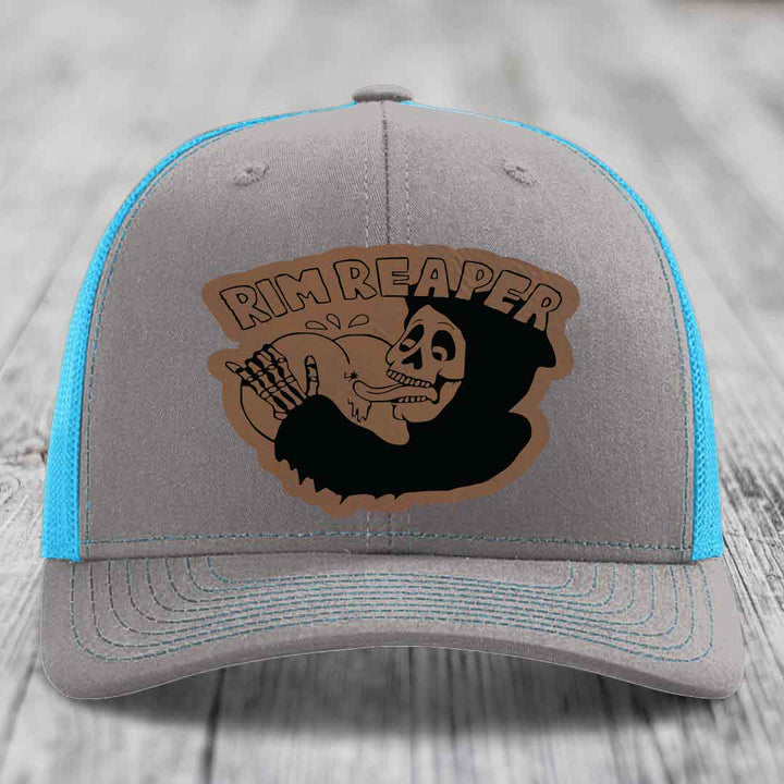 Grey trucker hat with blue mesh sides and a brown leatherette patch featuring a skull holding a golf club and the text &