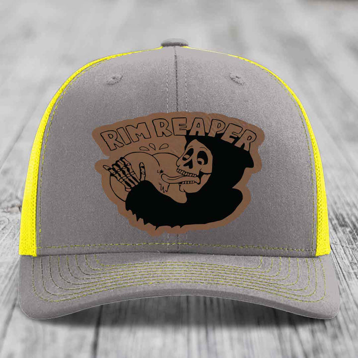 Grey trucker hat with yellow mesh and stitching, featuring a brown leatherette patch of a skeleton holding a basketball with &