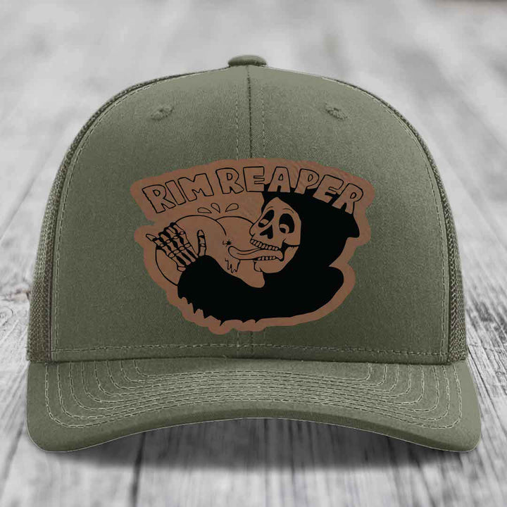 Olive green trucker hat with a brown leather patch featuring a skull holding a baseball and the text &