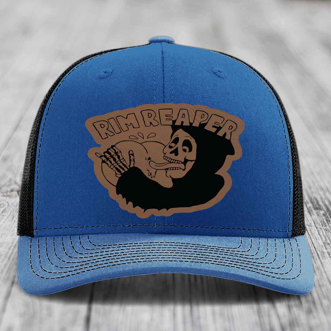Blue trucker hat with brown leatherette patch featuring skull holding baseball, text reads &