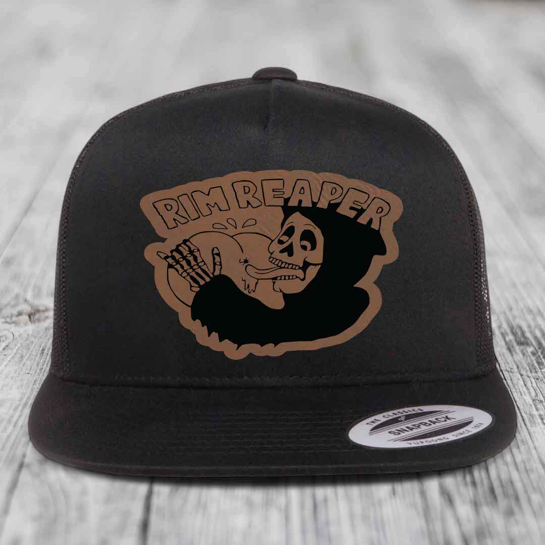 Black snapback trucker hat with brown leather patch featuring a skeleton holding a basketball and text &