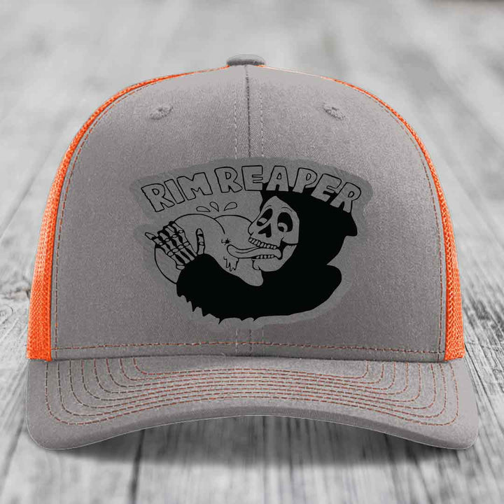 Grey trucker hat with orange mesh back and black skull graphic reading &