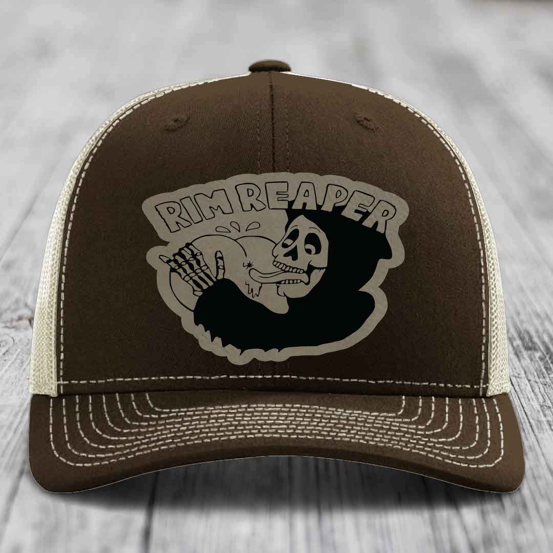 Brown trucker hat with white stitching and a black skull graphic that says &