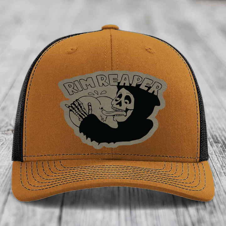 Tan trucker hat with black mesh back and gray skull patch reading &