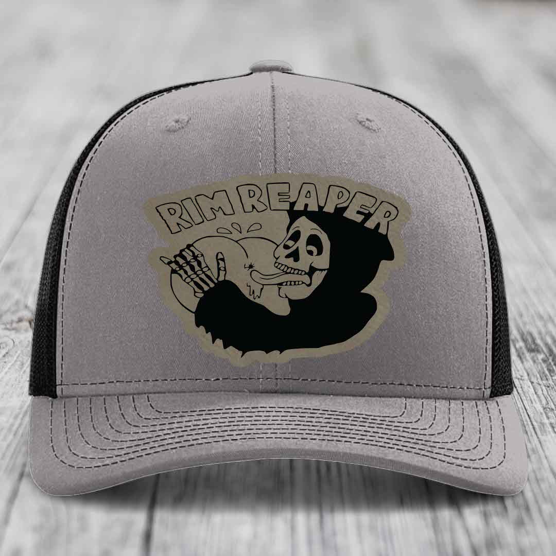 Grey trucker hat with black mesh back and a black skull-and-bones patch that says &