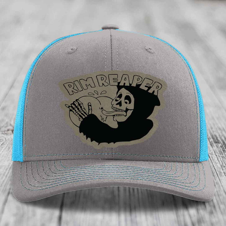 Grey trucker hat with blue mesh sides and a black skull graphic patch that says Rim Reaper.