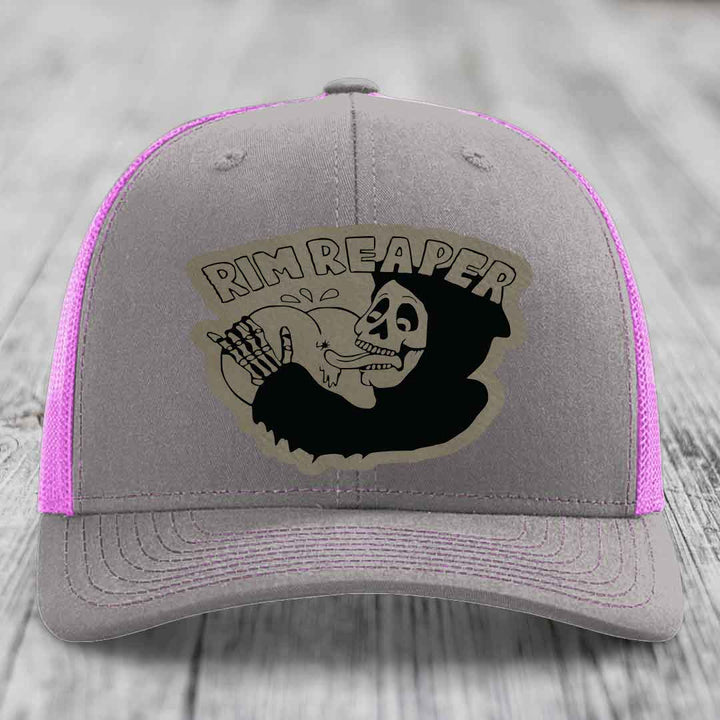 Grey trucker hat with pink mesh sides and a black skull graphic patch that says &