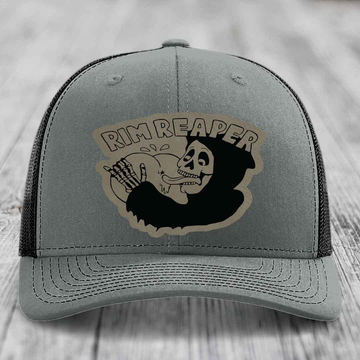 Grey trucker hat with black mesh back and a skull graphic patch that reads &