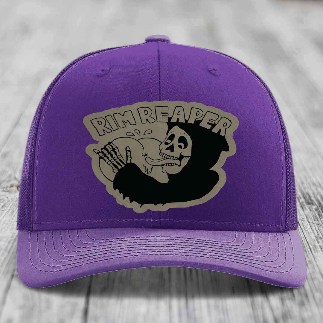 Purple trucker hat with a black and grey skull graphic patch that says &