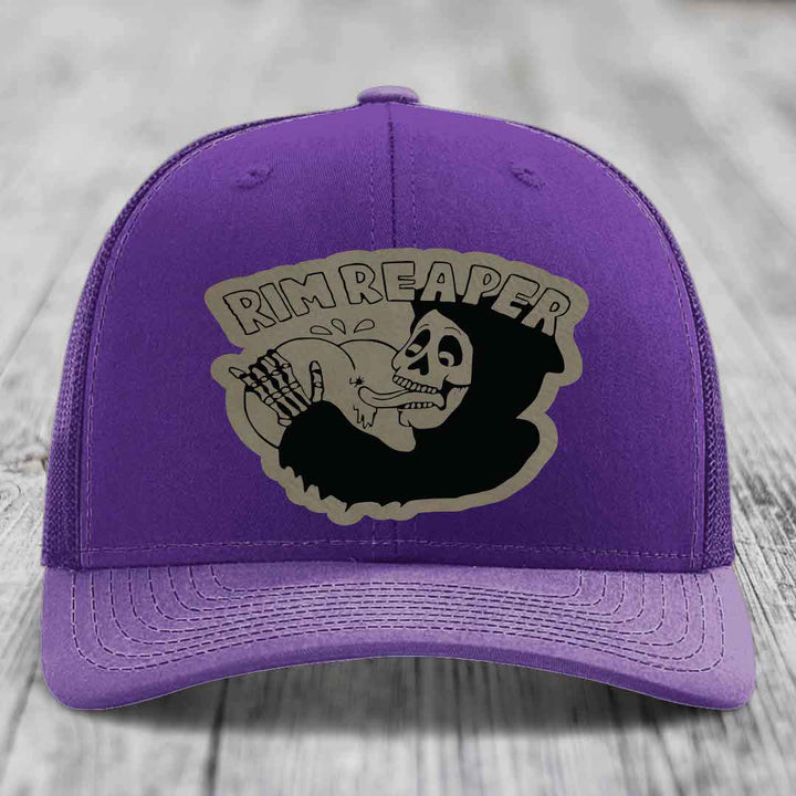 Purple trucker hat with a black and grey skull graphic patch that says &