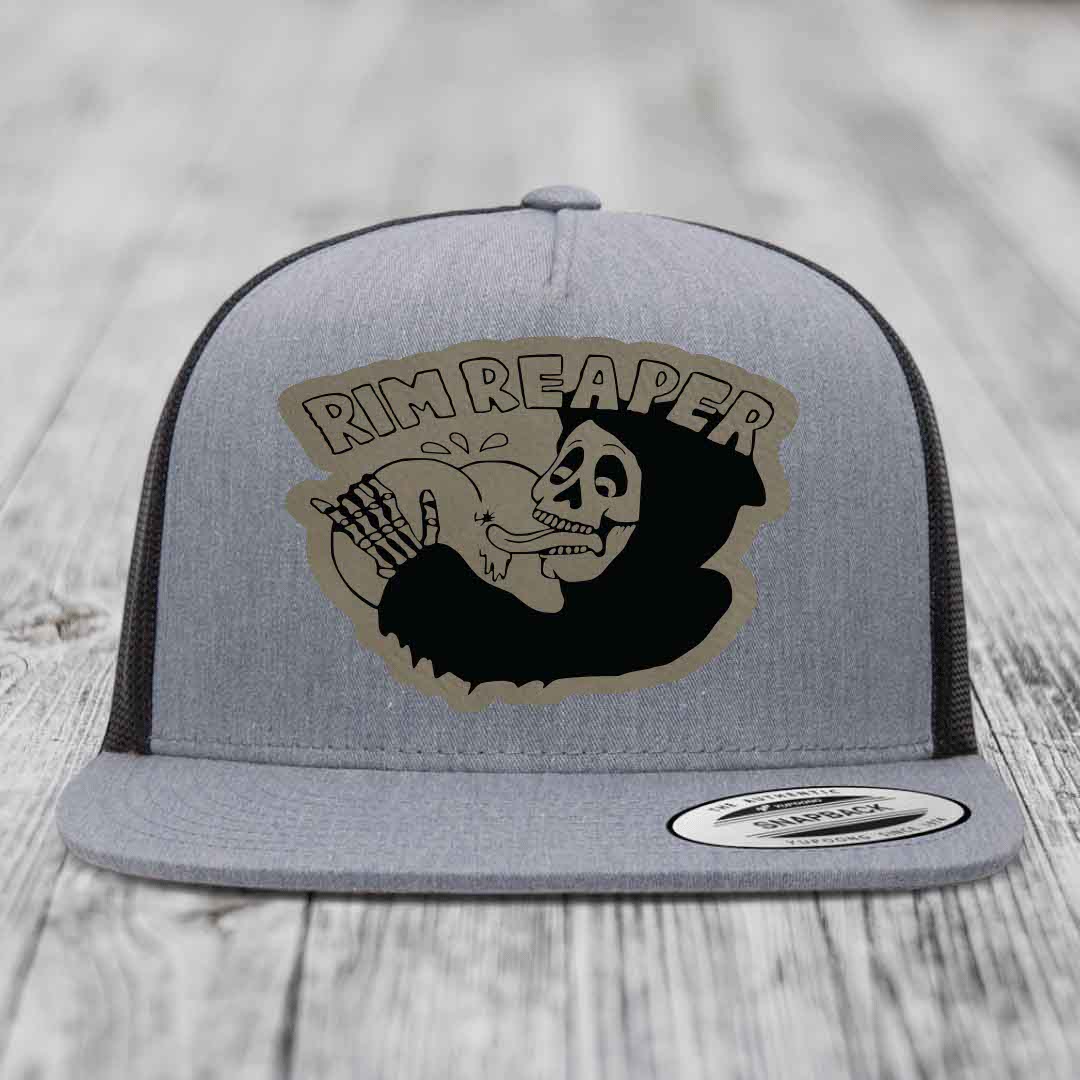 Grey trucker hat with black mesh back and a skull graphic patch that reads &