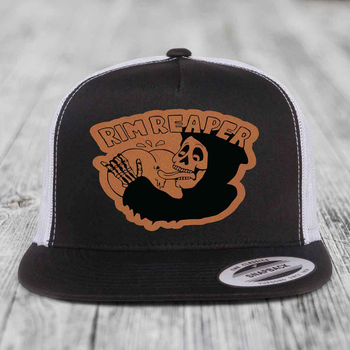 Black and white trucker hat with brown leather patch featuring a skeleton holding a golf club and text &
