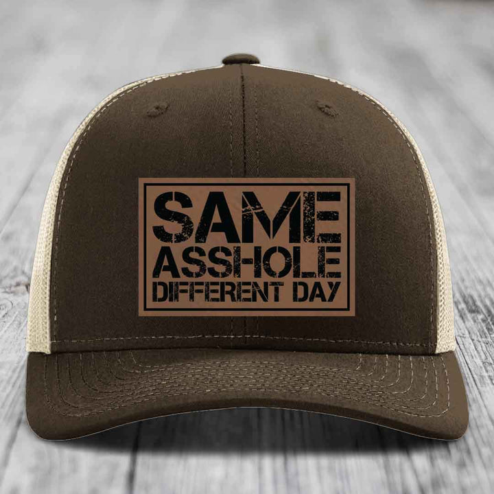 Brown trucker hat with beige mesh back and black text patch reading &