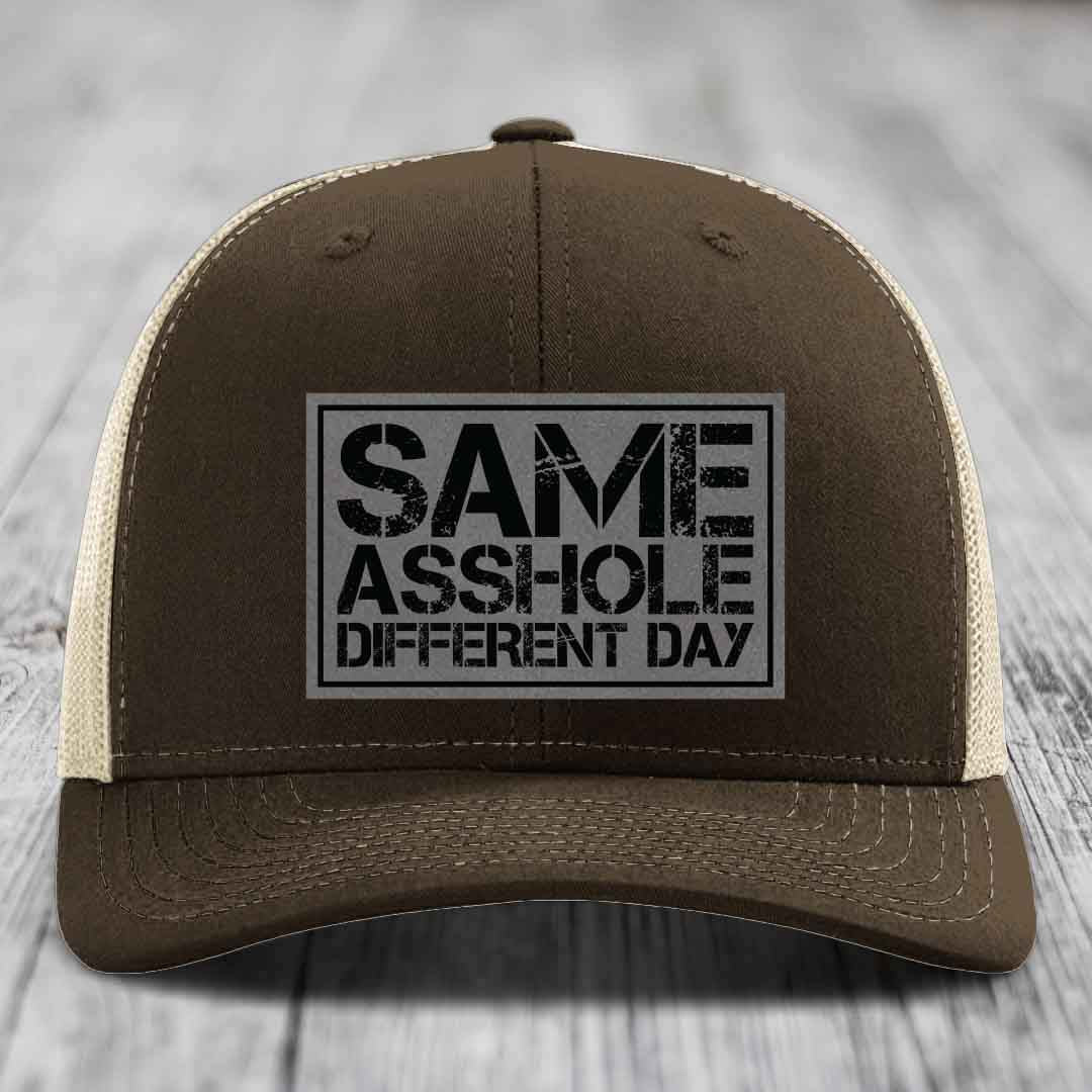 Brown trucker hat with beige mesh back and black embroidered patch reading &