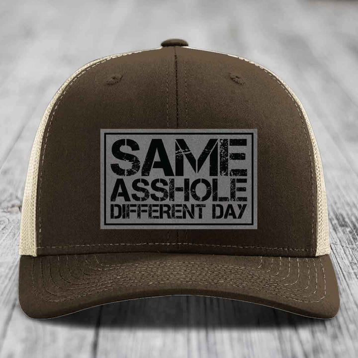 Brown trucker hat with beige mesh back and black embroidered patch reading &