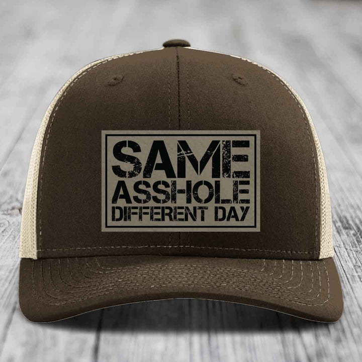 Brown trucker hat with beige mesh back and black text patch reading &