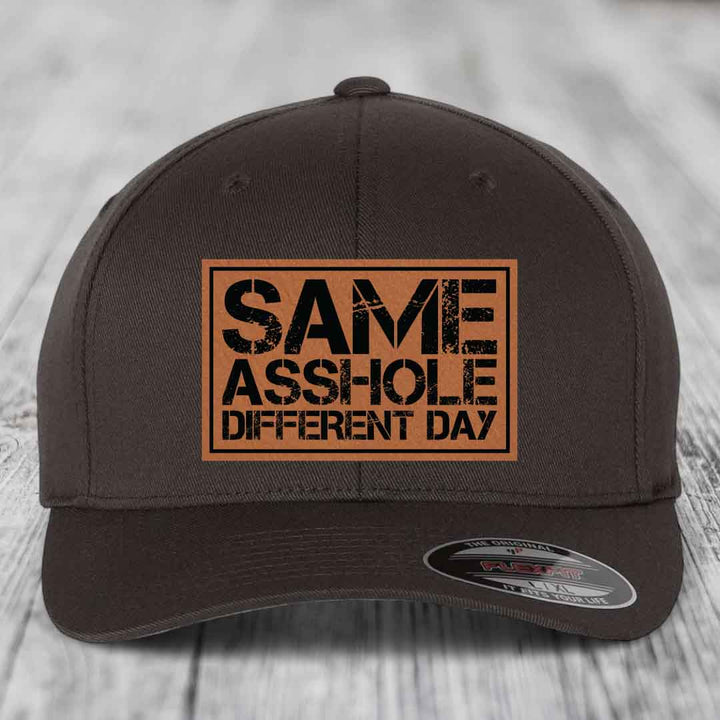 Dark brown baseball cap with a rectangular tan leatherette patch that reads &