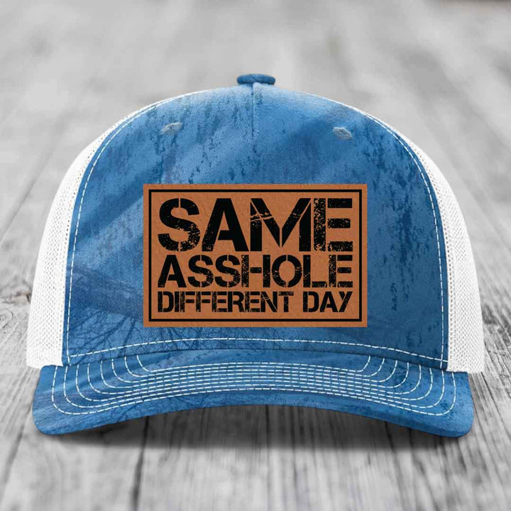 Blue and white trucker hat with a brown leather patch that reads &