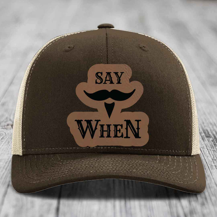 Brown trucker hat with beige mesh back and a brown leather patch that says &
