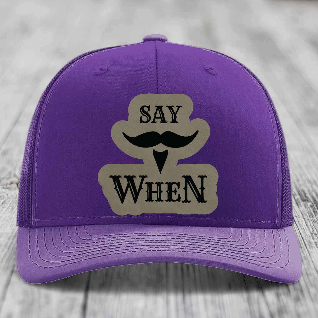 Purple trucker hat with a beige leatherette patch featuring &