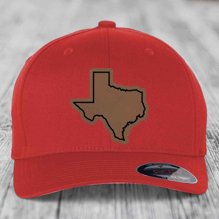Red baseball cap with brown Texas state outline patch on front, displayed on wooden surface.