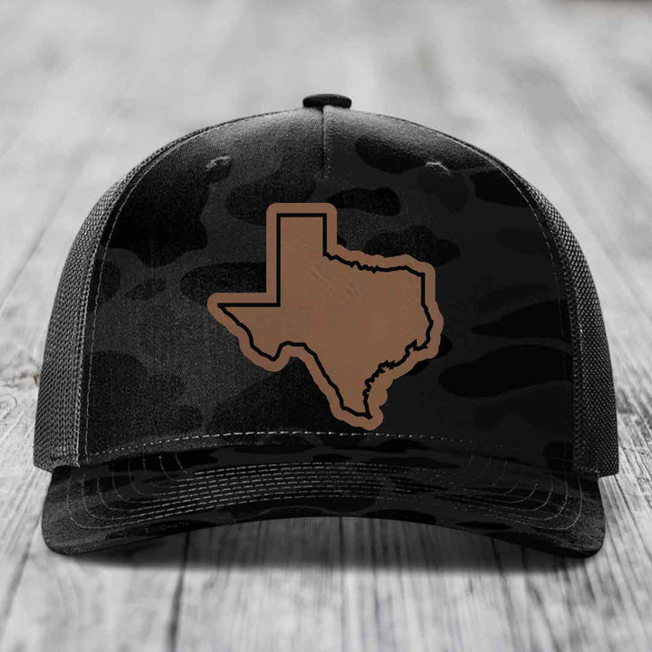 Black camouflage trucker hat with brown Texas state outline patch on front.