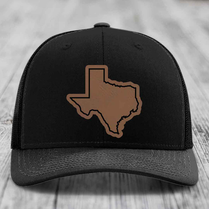 Black trucker hat with brown leatherette Texas state outline patch on front.
