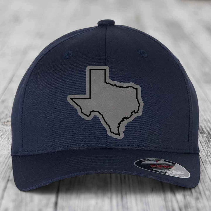 Dark blue baseball cap with gray Texas state outline patch on front, placed on wooden surface.