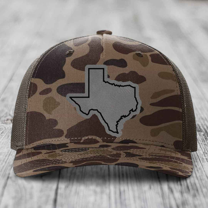 Camouflage trucker hat with gray Texas state outline patch on front.