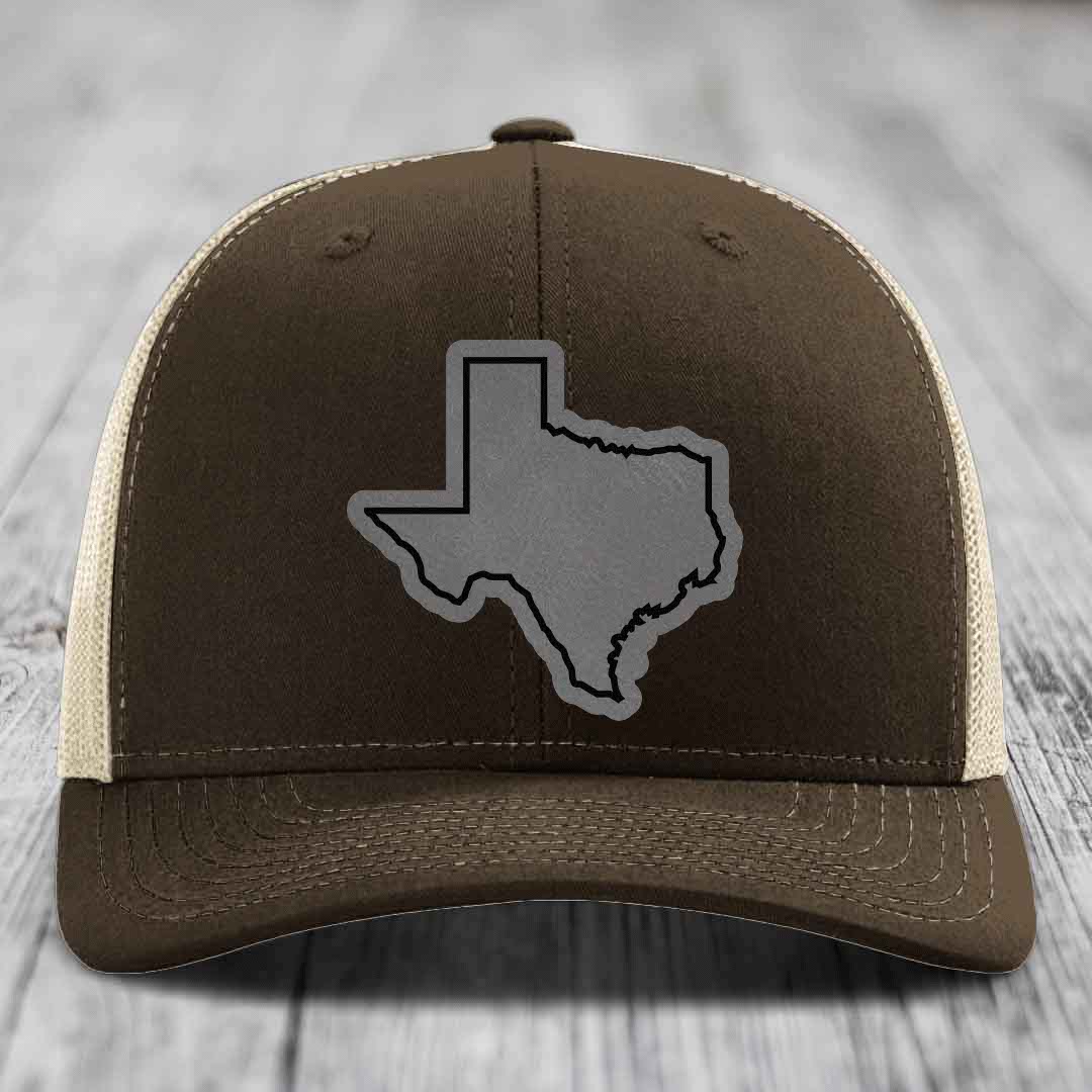 Brown trucker hat with grey Texas state outline patch on front, cream mesh sides.