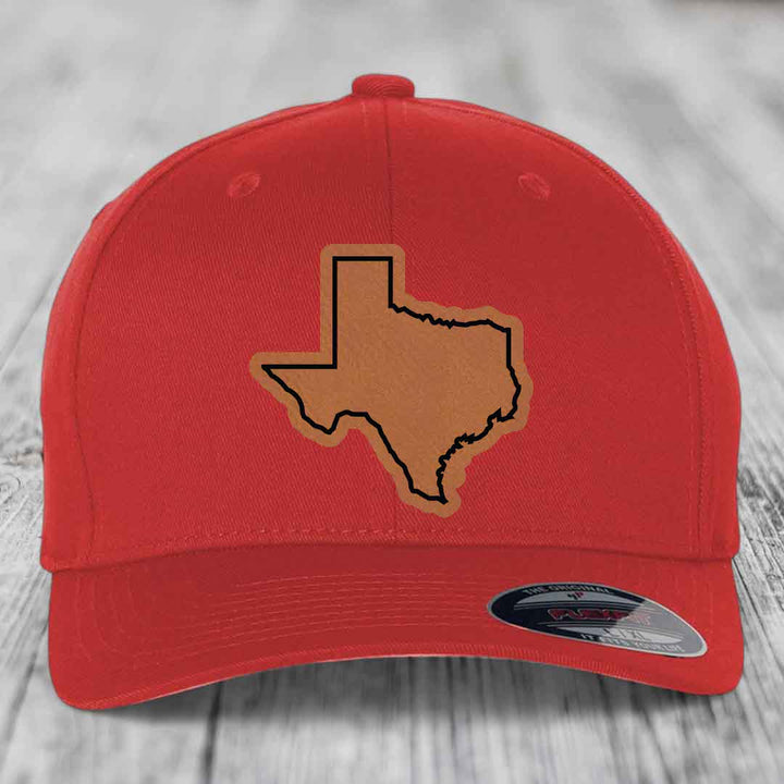 Red baseball cap with light brown Texas state outline patch on front, displayed on wooden surface.