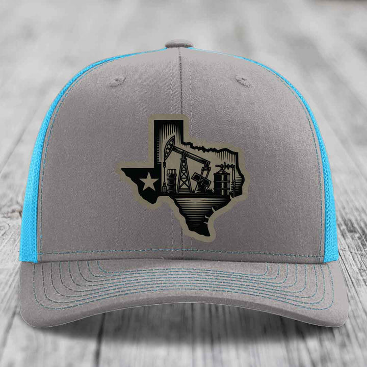 Grey trucker hat with blue mesh sides and a black Texas oilfield patch on front.