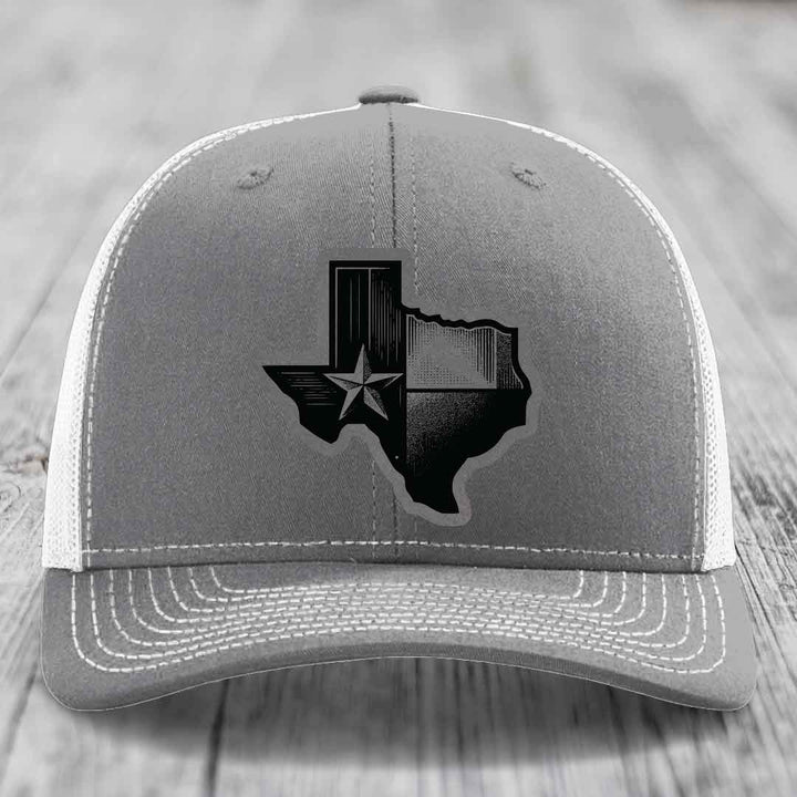 Grey trucker hat with black Texas-shaped patch featuring star and stripes design.