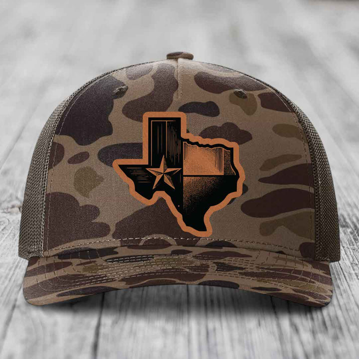 Camouflage trucker hat with Texas state flag patch on front, sitting on wooden surface.