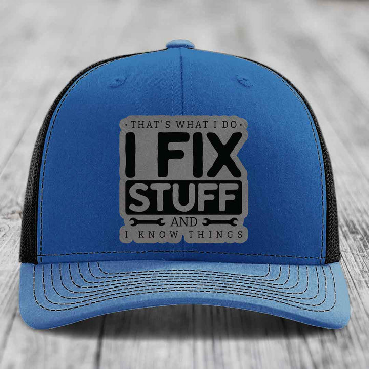Blue trucker hat with black mesh back and gray leatherette patch reading &