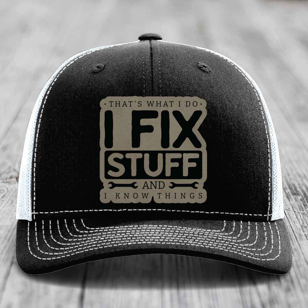 Black trucker hat with white mesh back and stitching, featuring a tan leatherette patch that reads &