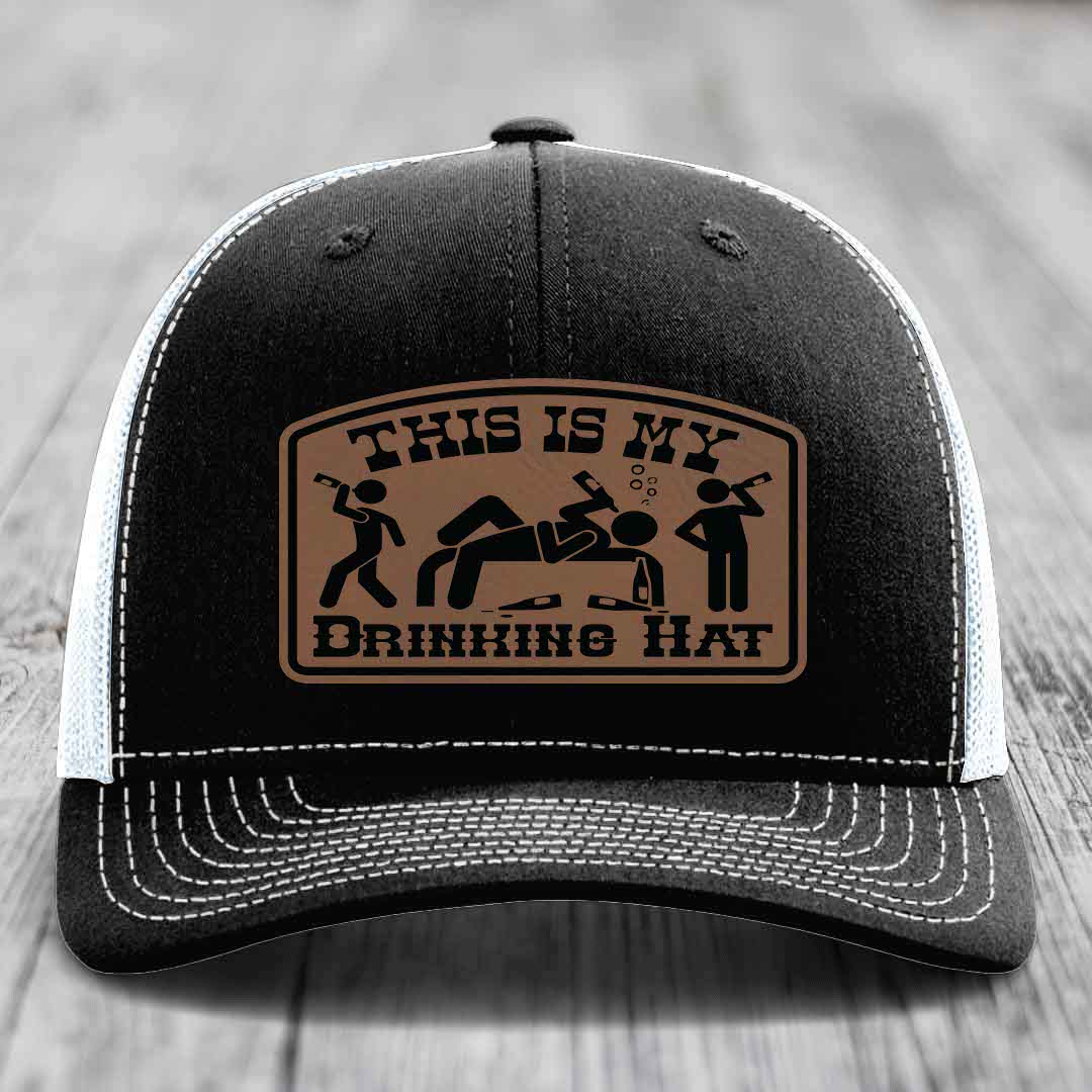 Black trucker hat with white mesh back and stitching, featuring a brown leatherette patch that reads &