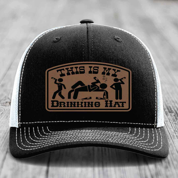 Black trucker hat with white mesh back and stitching, featuring a brown leatherette patch that reads &