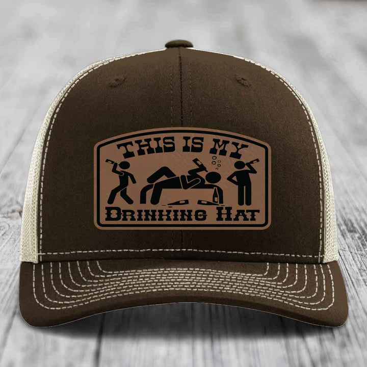 Brown trucker hat with beige mesh back and white stitching, featuring a tan leather patch that reads &