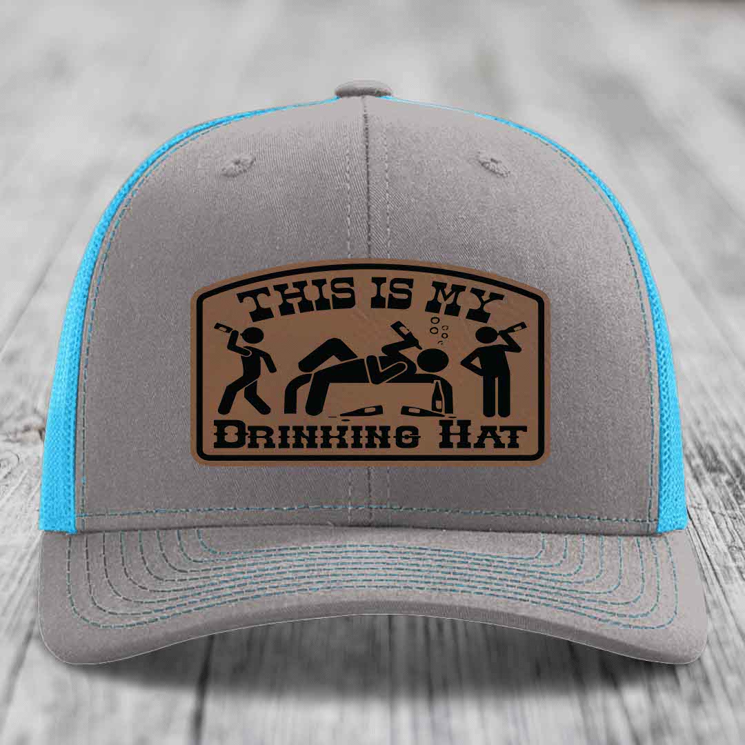 Grey trucker hat with blue mesh back and brown leather patch reading &