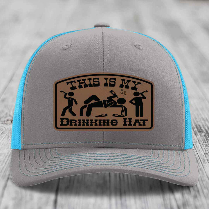 Grey trucker hat with blue mesh back and brown leather patch reading &