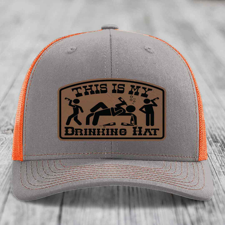Grey trucker hat with orange mesh back and a brown leather patch that reads &
