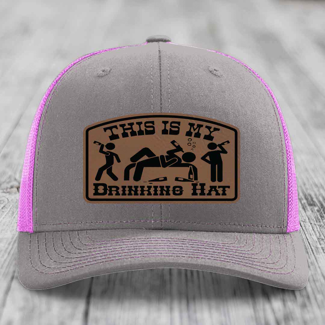 Grey trucker hat with pink mesh back and a brown leather patch that reads &