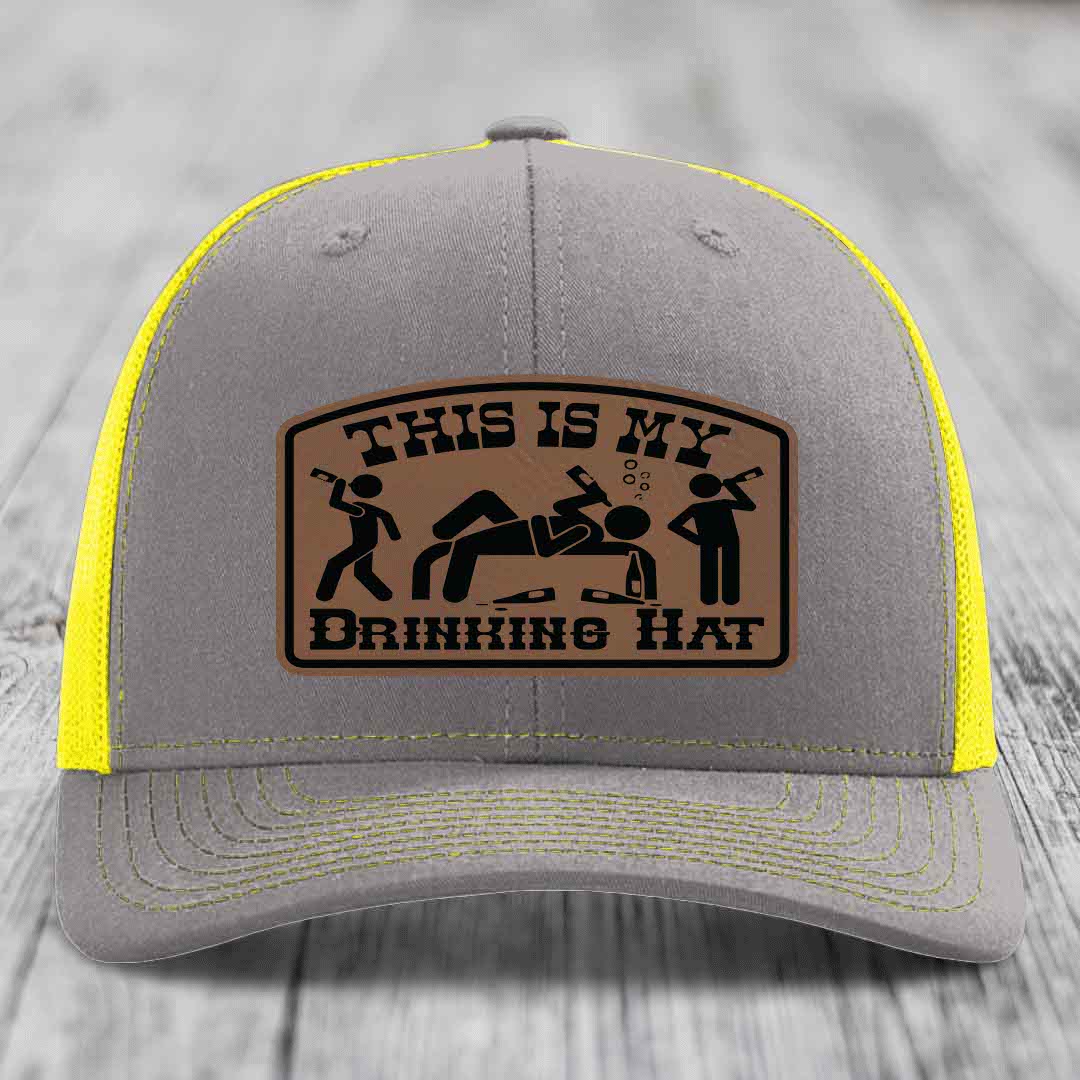 Grey trucker hat with yellow mesh and stitching, featuring a brown leather patch that reads &