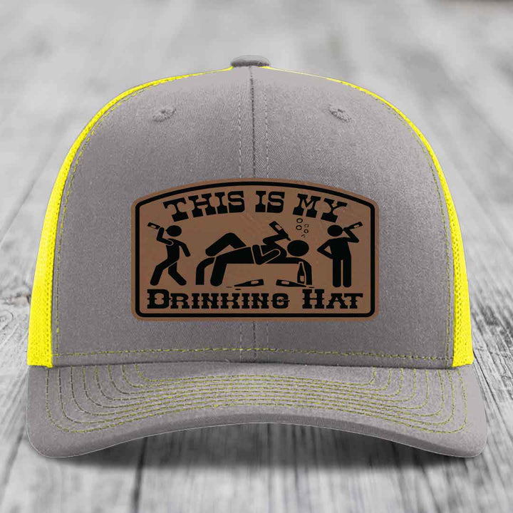 Grey trucker hat with yellow mesh and stitching, featuring a brown leather patch that reads &