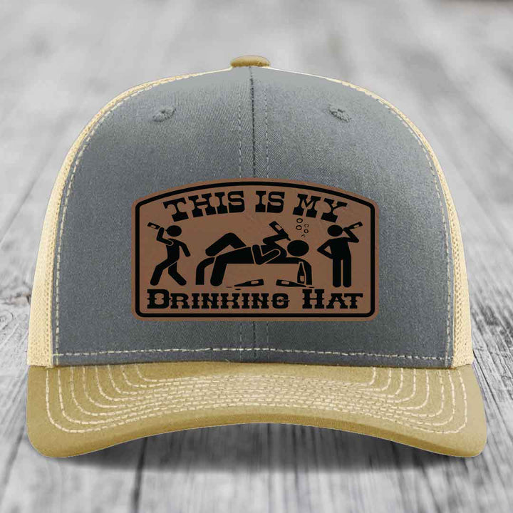 Grey and beige trucker hat with a brown leather patch that reads &