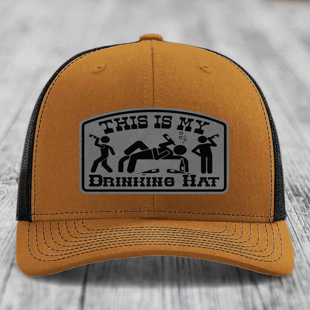 Tan trucker hat with black mesh back and a gray leatherette patch reading &