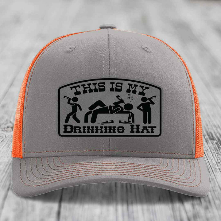 Grey trucker hat with orange mesh back and black patch reading &